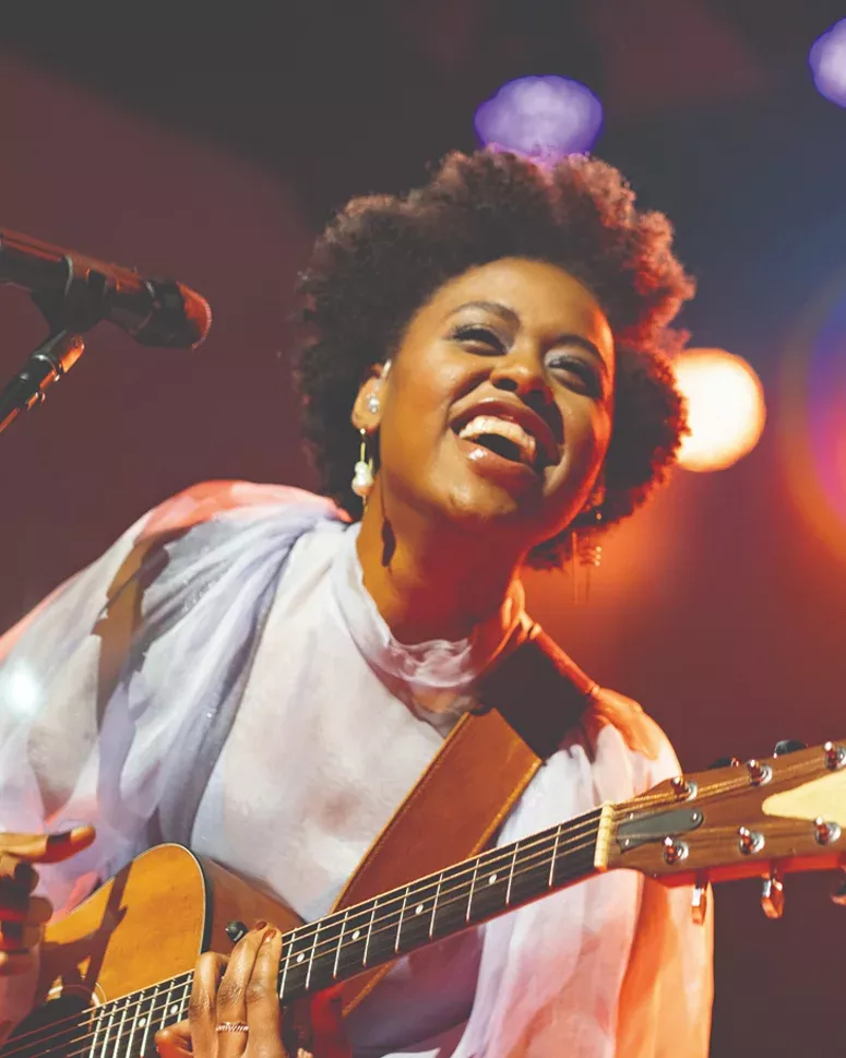 Woman playing guitar and smiling with a microphone, from an exclusive live event at The Strathmore.